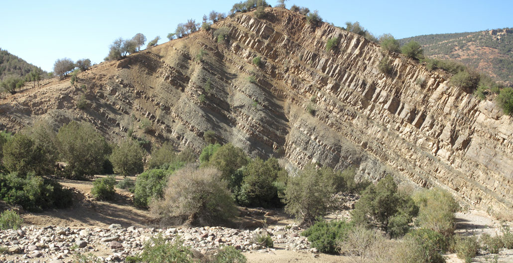 Angled layers of rock jut out of a desert landscape