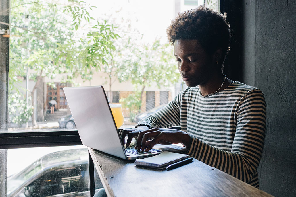 a young black man using a laptop at a coffee shop