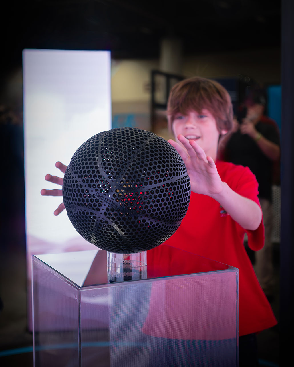 an airless basketball on display, a boy in a red shirt is reaching for the ball