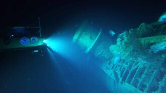 a photo of a subermisible lighting up a shipwreck underwater