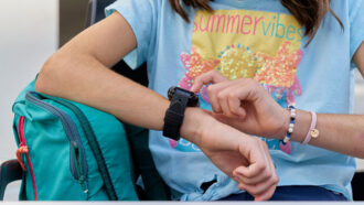 a close up photo of a teen checking her smartwatch, only her torso and arms are in the picture