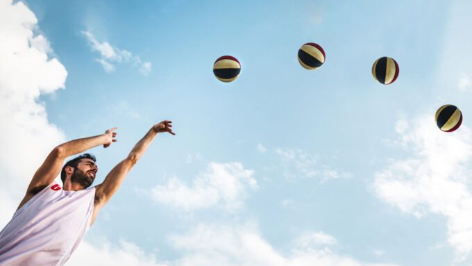 a composite photo showing a guy shooting a basketball in an arc, the basketball is shown four times in consecutive positions, showing the shape of the arc