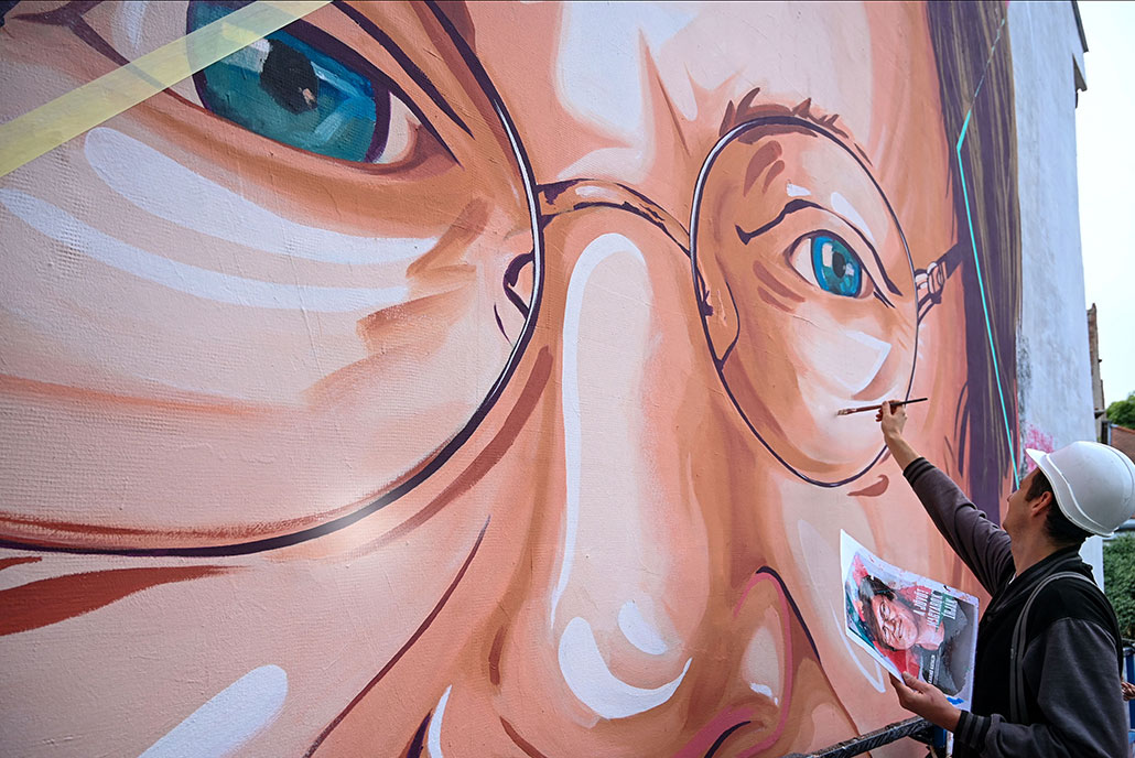 A member of 'The colorful city' artist group works on the painted portrait of Hungarian-American scientist Katalin Kariko, on a firewall in Budapest on August 28, 2021, amid the ongoing coronavirus Covid-19 pandemic.