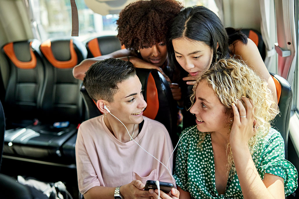 four friends huddle together to listen to music on a bus