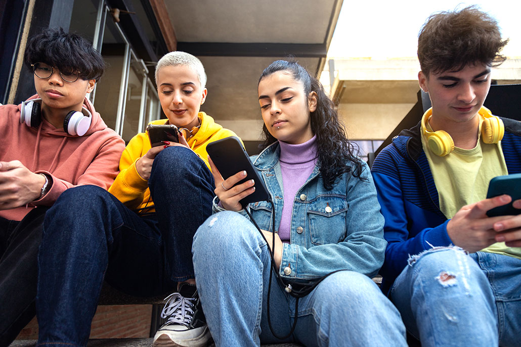 a line of friends sitting on a bench, all of them are looking at their smartphones