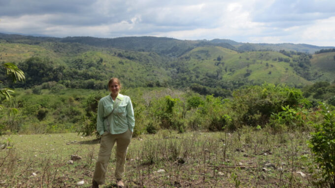 a young woman stands on a green hilly landscape under a blue sky