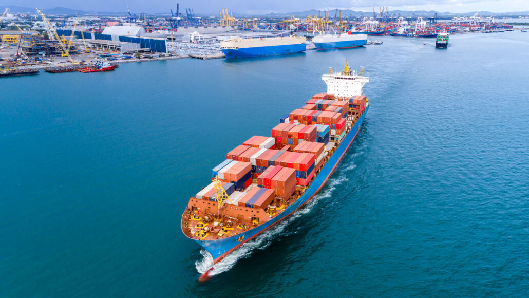 an aerial view of a loaded container ship sailing away from a harbor