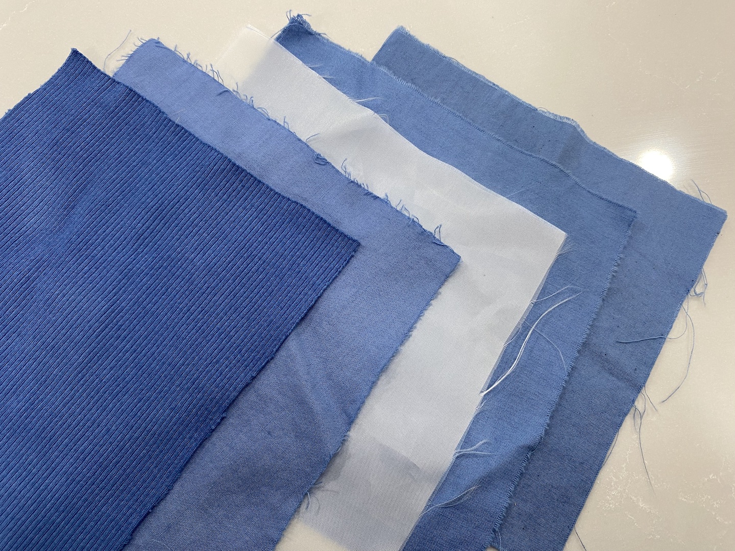 five square pieces of fabric are laid out, four of them died different shades of blue and one white