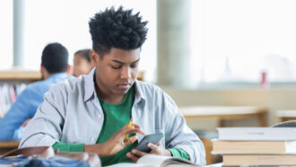 a teen boy uses a calculator at a desk covered in books