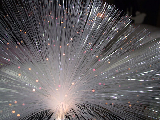 a bunch of fiber optic cables fanned out in a half sphere shape, the end of each clear cable stands out as bright dot of light