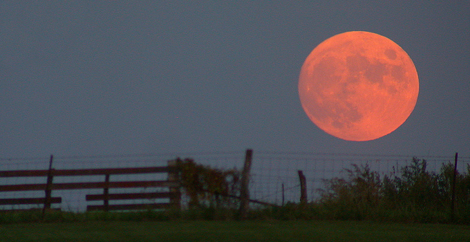 A reddish full moon hangs in the dim sky near the horizon